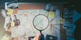 Hand holding magnifying glass over investigation board