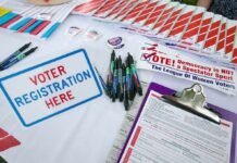 Voter registration table with forms, pens, and informational materials