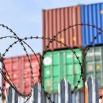 Barbed wire fence in front of stacked shipping containers