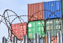 Barbed wire fence in front of stacked shipping containers