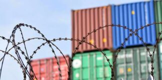 Barbed wire fence in front of stacked shipping containers