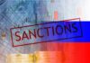 Sanctions text over financial chart and flag with coin stacks