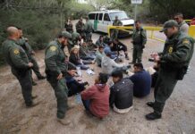 Border agents surround a seated group near a van