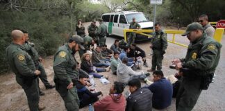 Border agents surround a seated group near a van