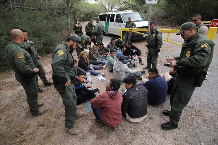 Border agents surround a seated group near a van
