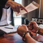 Handcuffed suspect at interrogation table with officer pointing