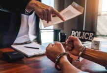 Handcuffed suspect at interrogation table with officer pointing