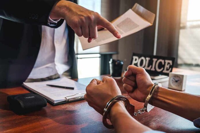 Handcuffed suspect at interrogation table with officer pointing