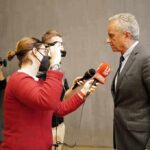 man in suit being interviewed by reporters
