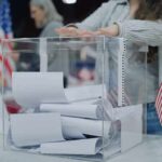 Person casting a ballot into a clear box at a polling station