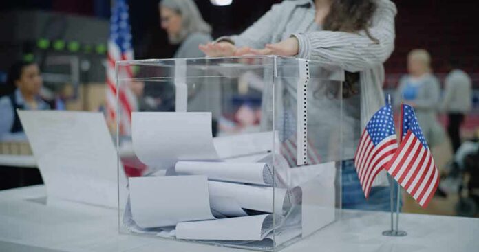 shutterstock_2454758129-3 Person casting a ballot into a clear box at a polling station