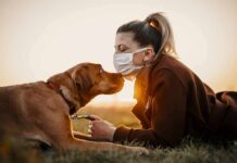 Woman in mask touching noses with brown dog at sunset