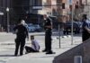 Police officers detain a seated man on a city sidewalk
