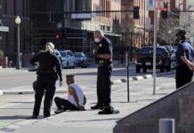 Police officers detain a seated man on a city sidewalk