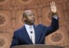 Speaker in suit addressing audience at podium with hand raised