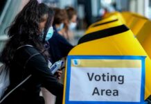 voter wearing a mask using a yellow ballot box