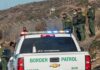 Border Patrol agents gather near fence with patrol trucks
