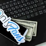 Smartphone with OnlyFans sticker and cash on a laptop keyboard