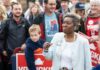 Woman speaking at a public rally surrounded by supporters