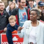 Woman speaking at a public rally surrounded by supporters