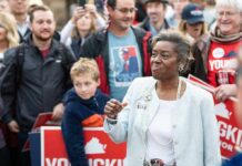 Woman speaking at a public rally surrounded by supporters