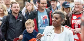 Woman speaking at a public rally surrounded by supporters