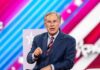 Greg Abbott speaking on stage in a suit against a colorful striped backdrop