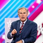 Greg Abbott speaking on stage in a suit against a colorful striped backdrop