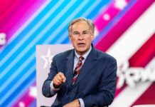 Greg Abbott speaking on stage in a suit against a colorful striped backdrop