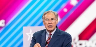 Greg Abbott speaking on stage in a suit against a colorful striped backdrop
