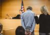 Defendant in handcuffs stands before a judge in a courtroom