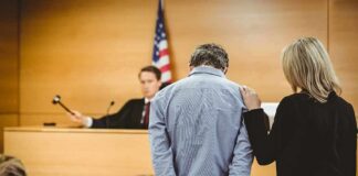 Defendant in handcuffs stands before a judge in a courtroom