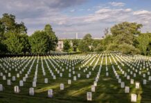 Rows of white headstones in a cemetery under a partly cloudy sky