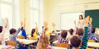 Students raise hands in a classroom with a teacher at the front