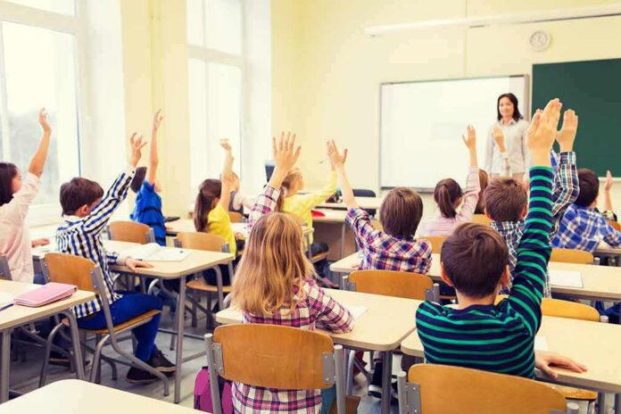 Students raise hands in a classroom with a teacher at the front