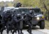 Tactical police team advances from armored vehicle with shields and rifles