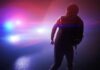 silhouetted person in front of police car with flashing lights