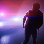 silhouetted person in front of police car with flashing lights
