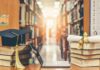 Graduation cap on books beside laptop and diploma in library aisle