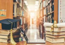 Graduation cap on books beside laptop and diploma in library aisle