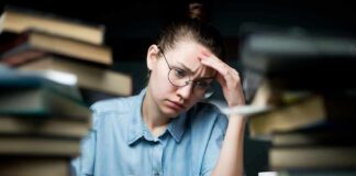 Student with glasses studying amid stacks of books