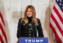 woman speaking at podium with microphones and US flags