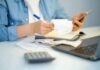 Person reviewing receipts with phone, notebook, and laptop