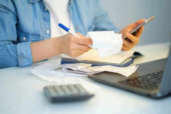 Person reviewing receipts with phone, notebook, and laptop