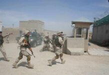 Soldiers in desert uniforms run past a checkpoint amid dust