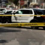 Police tape cordoning off street with patrol SUVs behind