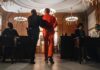 Prisoner in orange jumpsuit escorted by officer in a courtroom