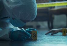 forensic investigator in protective suit examining crime scene markers