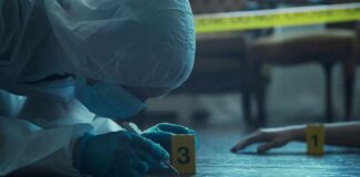 forensic investigator in protective suit examining crime scene markers