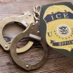 ICE officer badge and handcuffs on wooden surface